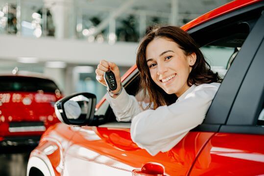 Junge Frau im roten Pkw beim Auto verkaufen